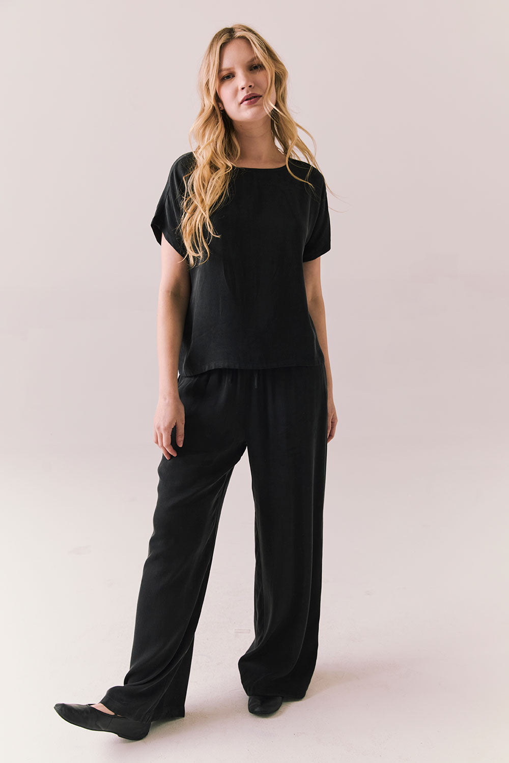 Full front view of woman wearing Davis tee in true black and matching Lee Pant against a plain background