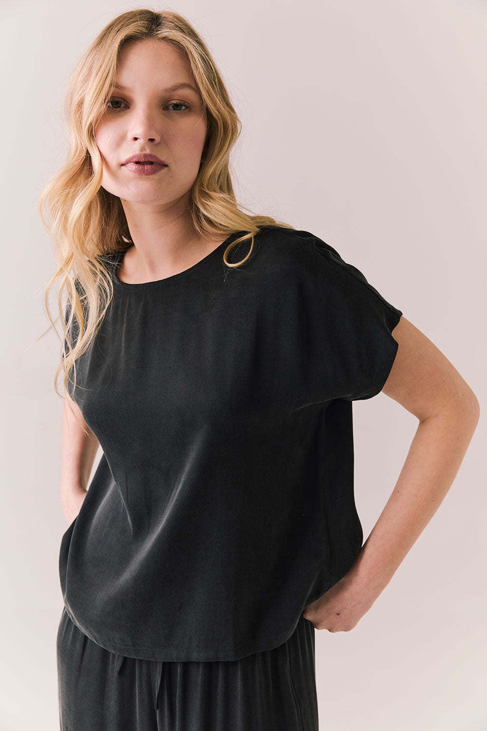 Side view of woman wearing Davis tee in true black and matching Lee Pant against a plain background