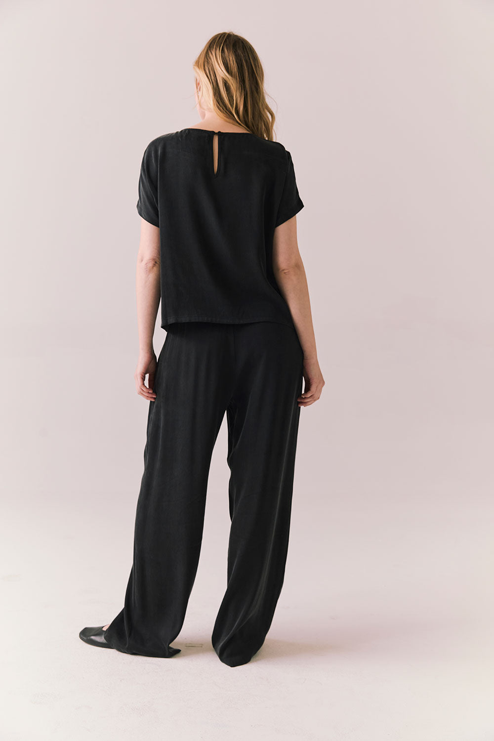 Full back view of woman wearing Davis tee in true black and matching Lee Pant against a plain background