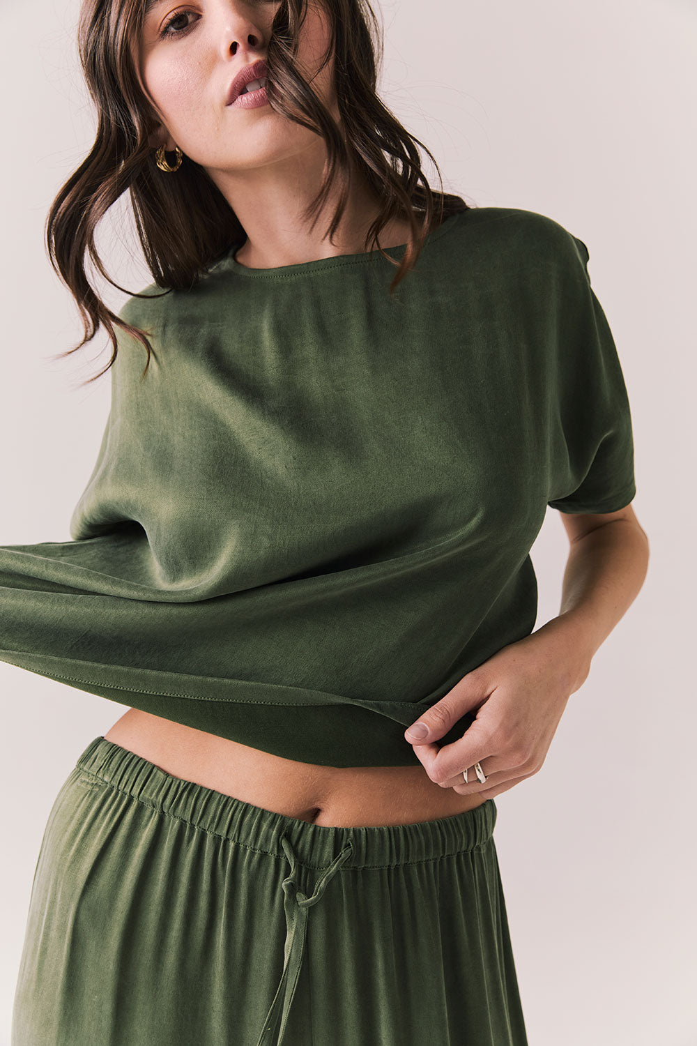 Front view of woman wearing the Davis tee in bronze green with matching Lee trousers, shot on a white background.
