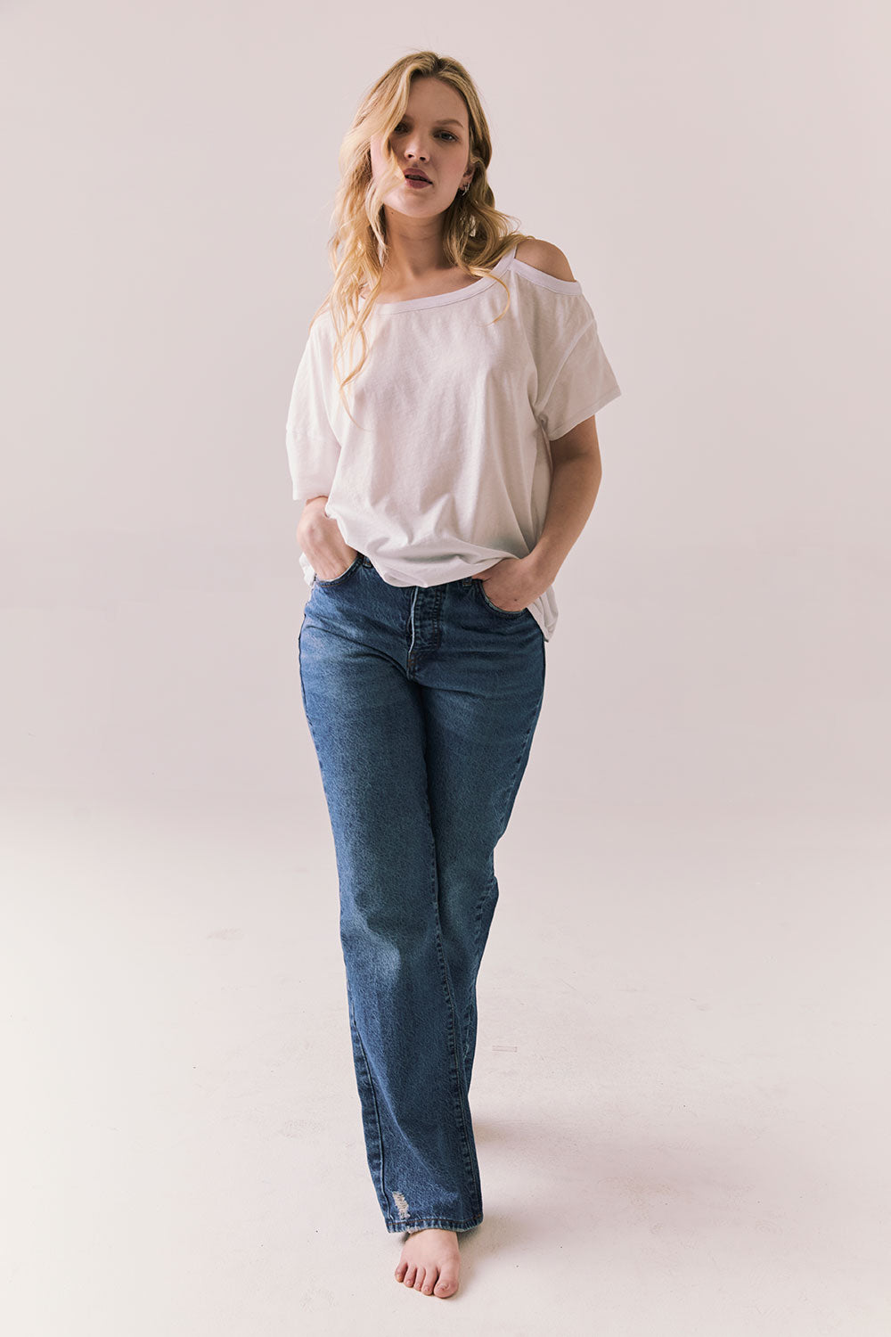Full front view of Northridge Tee in white with cold shoulder cutout and flowy fit and blue jeans against a plain background
