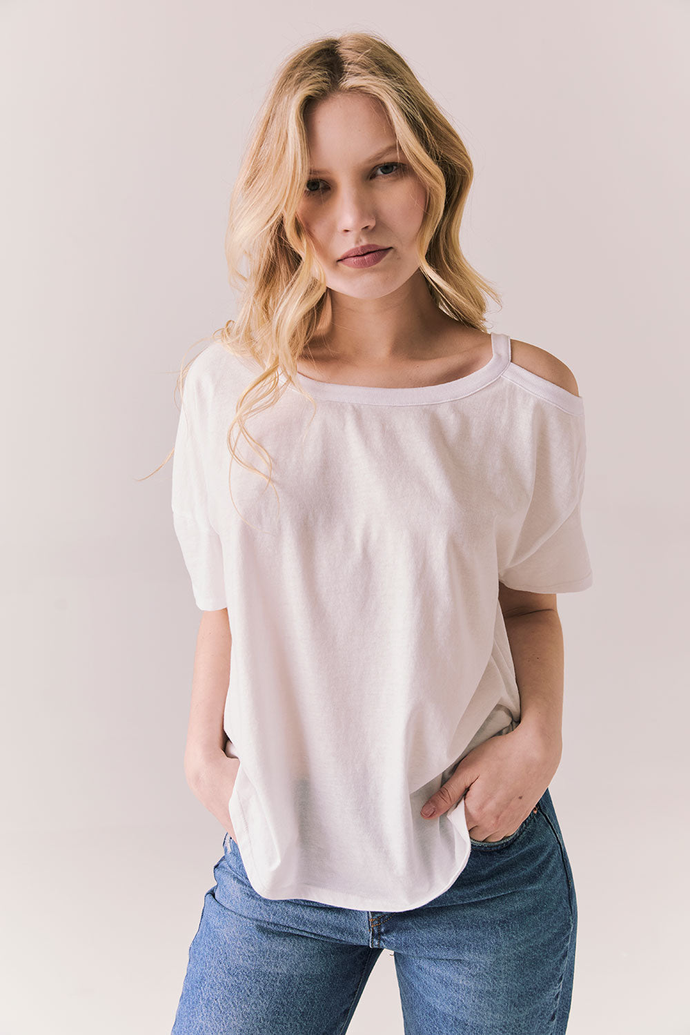 Front view of Northridge Tee in white with cold shoulder cutout and flowy fit and blue jeans against a plain background