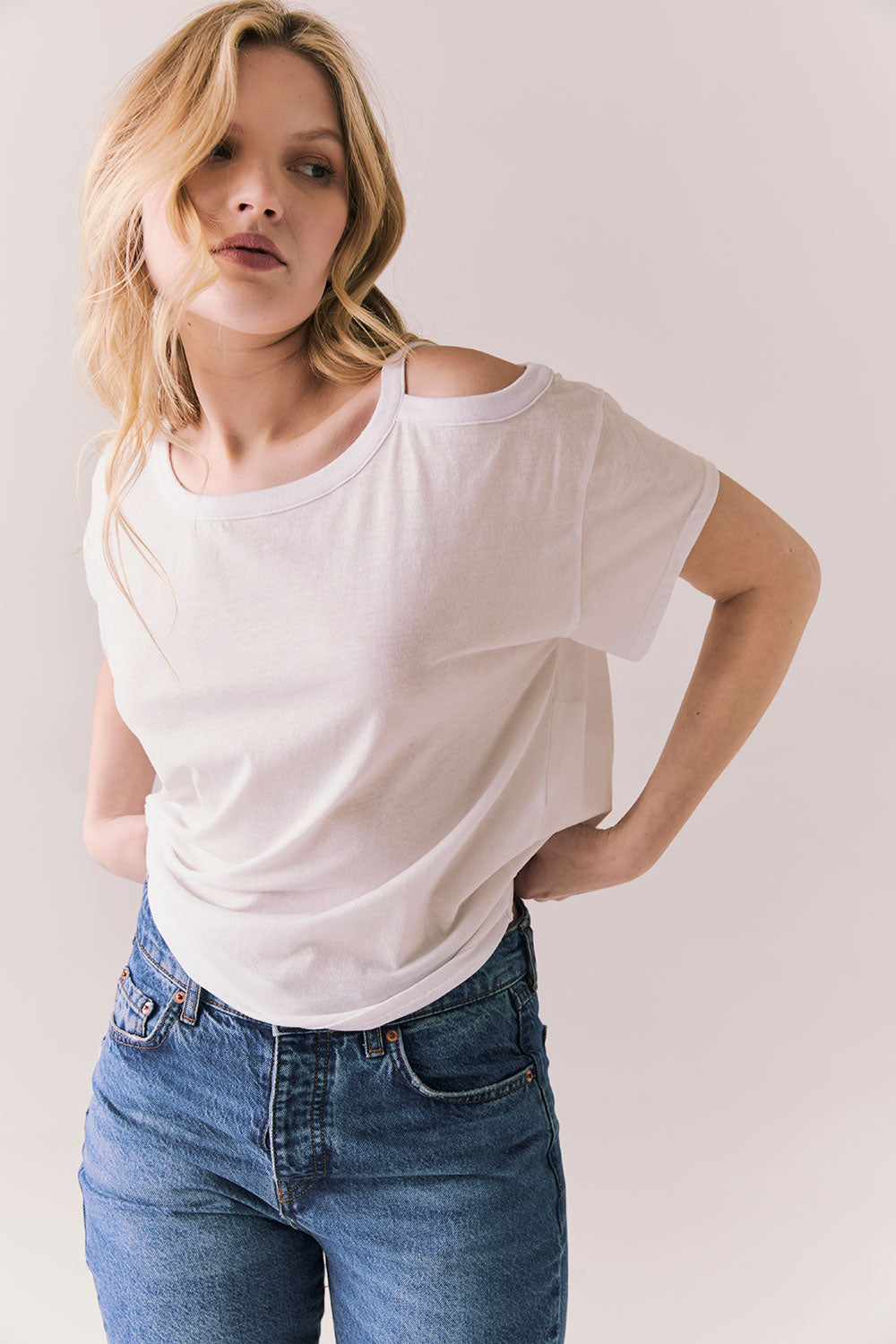 Front view of Northridge Tee in white with cold shoulder cutout and flowy fit and blue jeans against a plain background