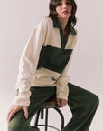 Woman wearing the color-blocked Chico Long Sleeve White and Green Rib Pullover and green pants sitting on a stool against a plain background