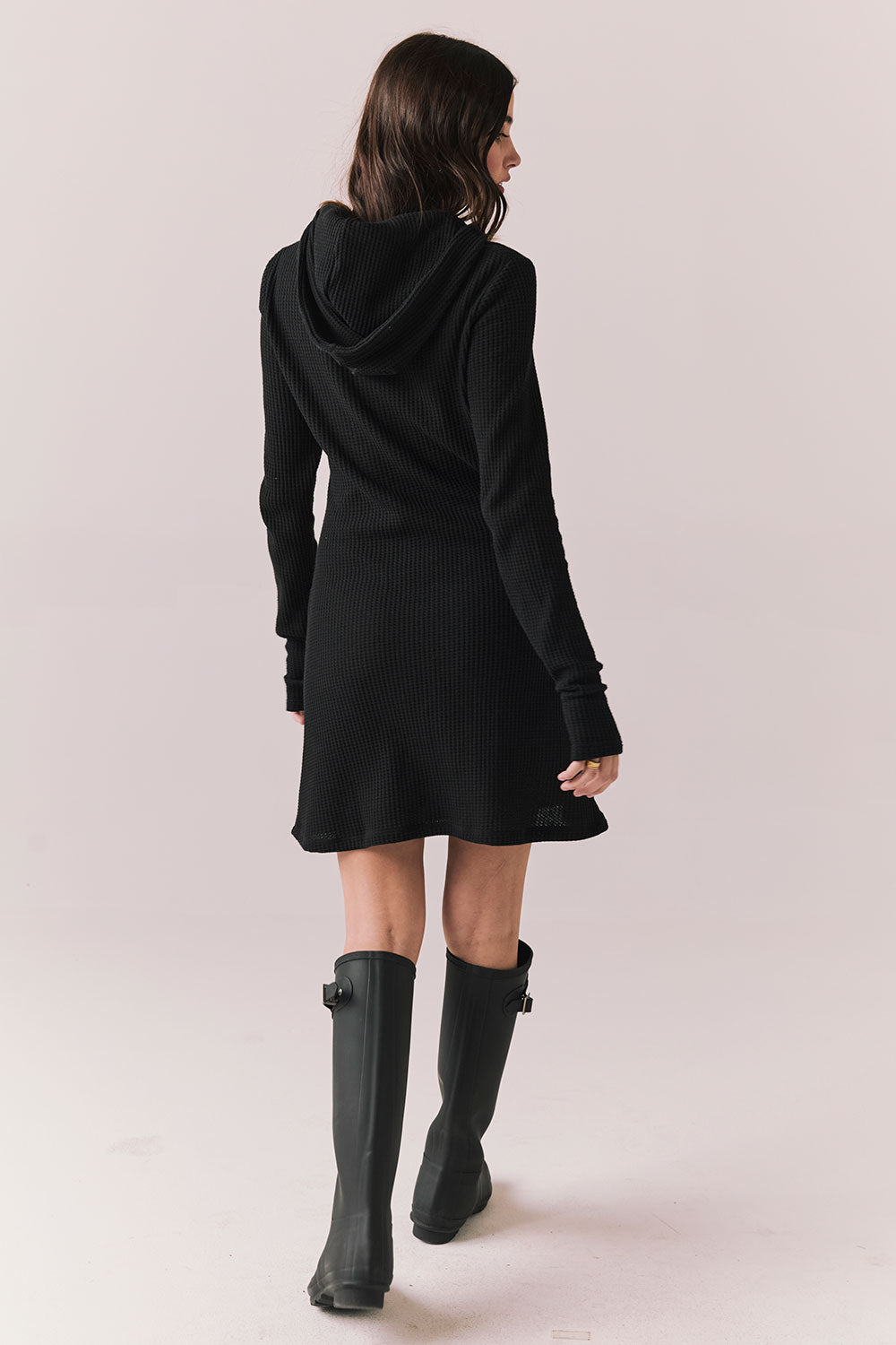 Back full body view of model in Merced Hoodie Dress in True Black with hood against a plain background