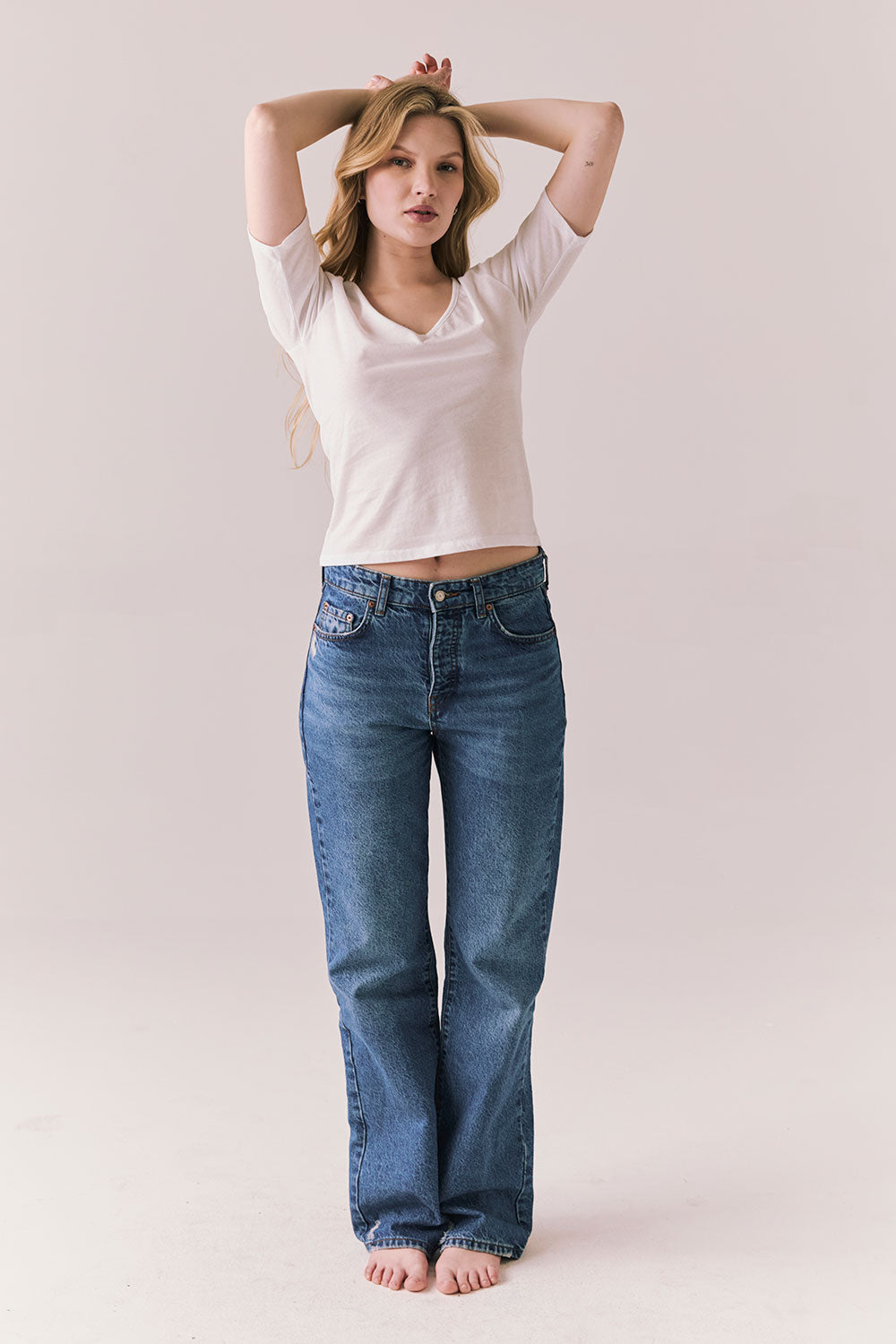 Full body view of model wearing Fresno tee in white with scoop neckline and fitted silhouette and blue jeans against a plain background