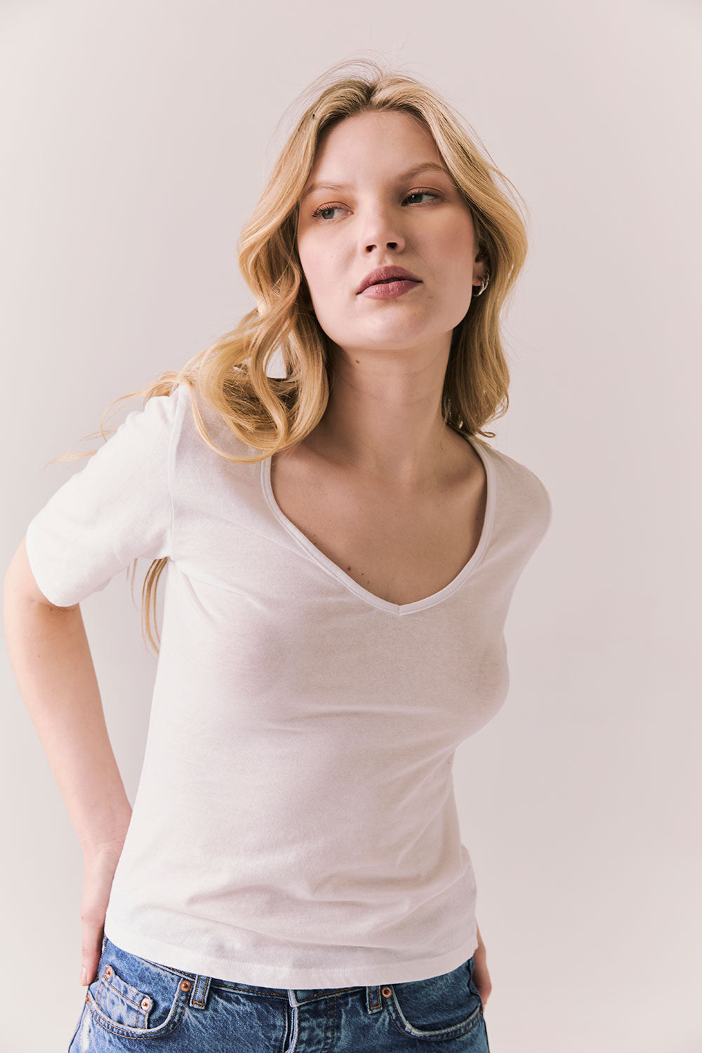 Front view of model wearing Fresno tee in white with scoop neckline and fitted silhouette and blue jeans against a plain background