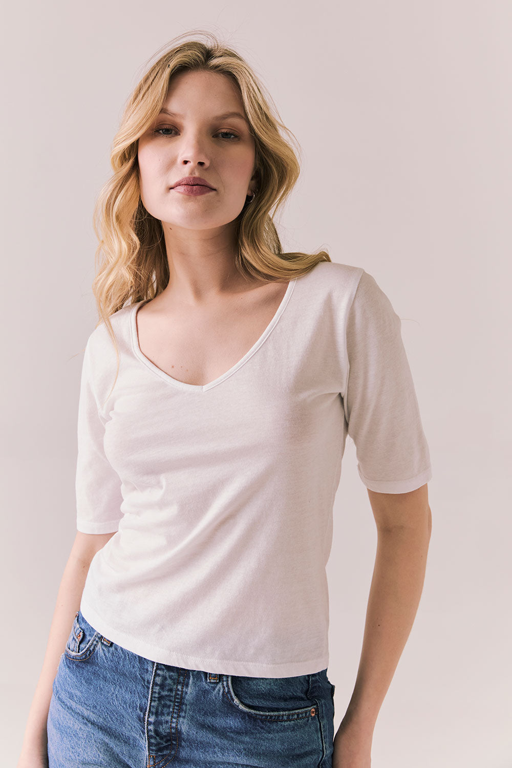 Front view of model wearing Fresno tee in white with scoop neckline and fitted silhouette and blue jeans against a plain background