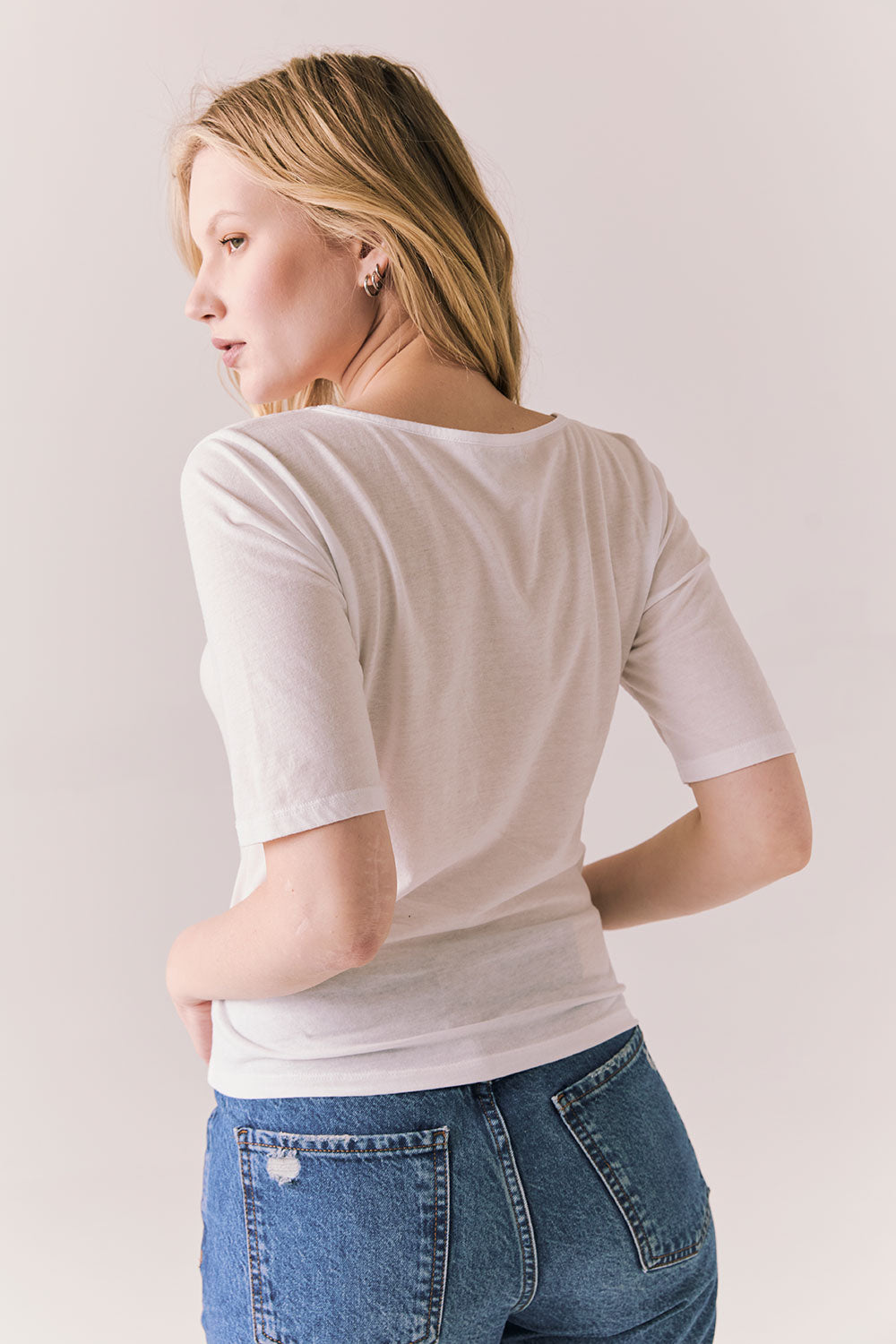 Back view of model wearing Fresno tee in white with scoop neckline and fitted silhouette and blue jeans against a plain background
