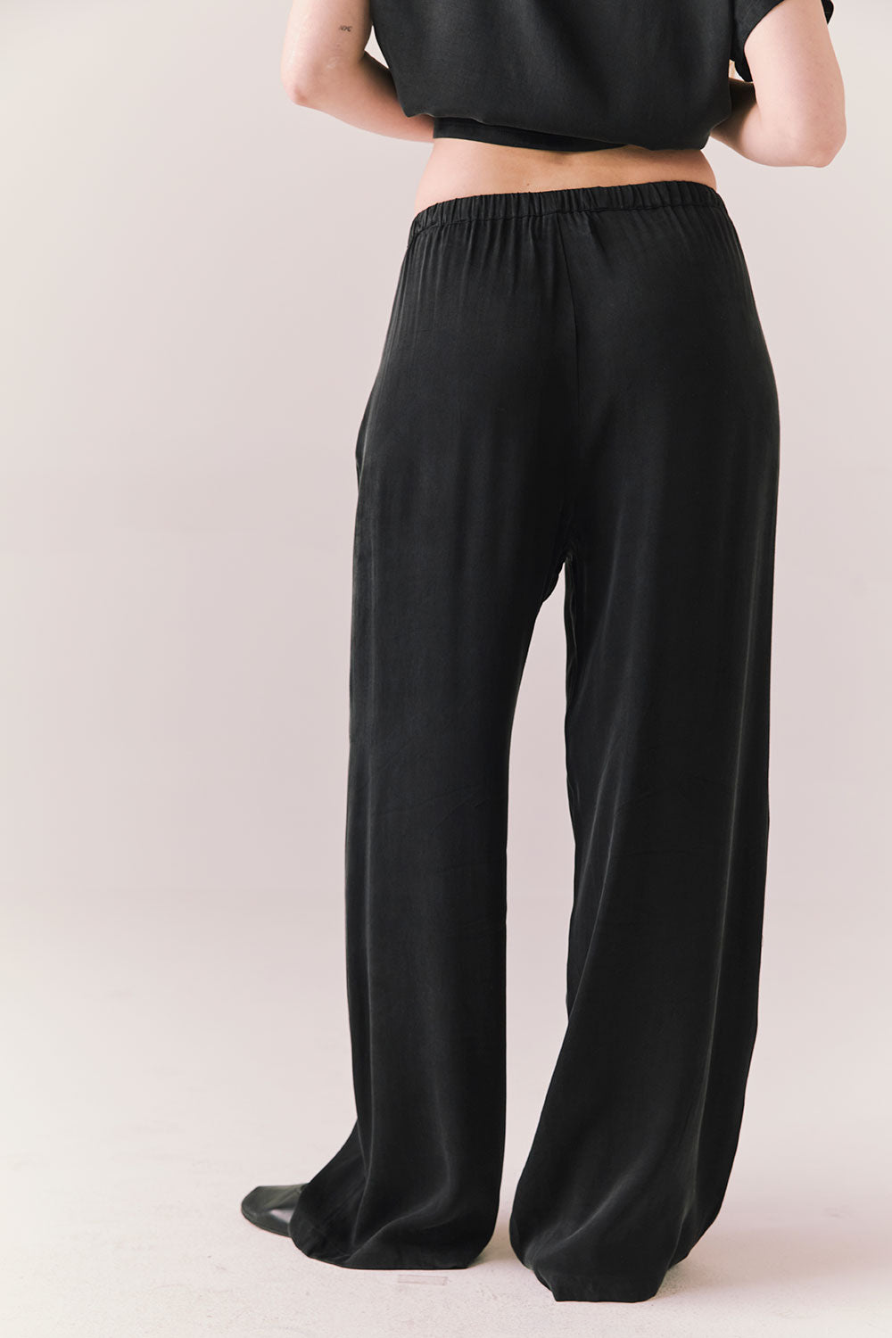 Back view of model wearing Lee Trouser in True Black with high-rise fit and wide-leg silhouette with matching Davis top against a plain background