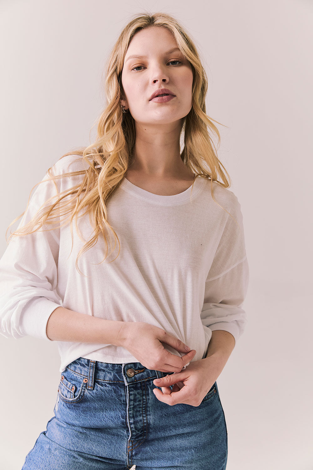 Front view of women wearing the Hartt long sleeve in white with cotton texture and clean silhouette and blue jeans against a plain background