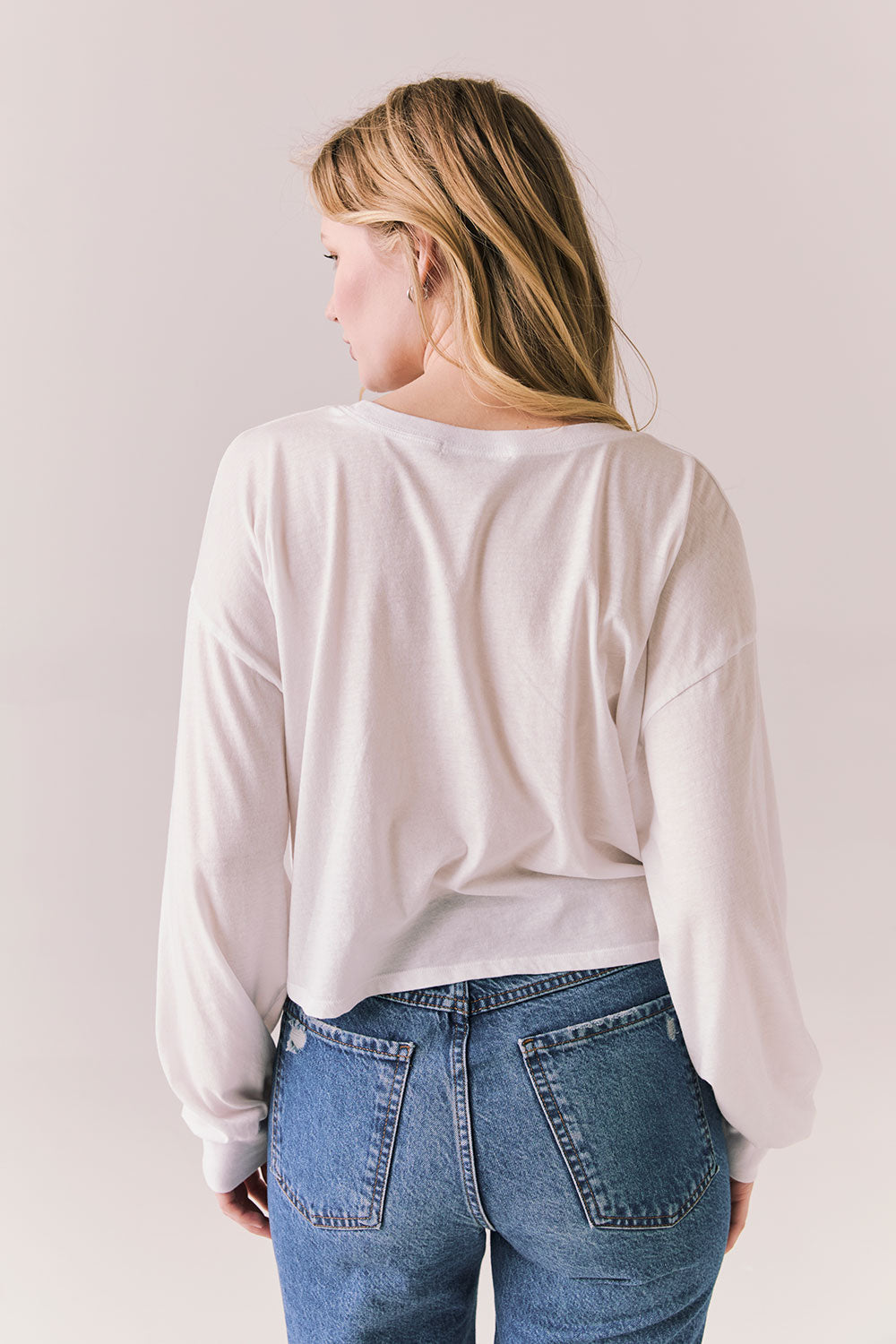 Back view of women wearing the Hartt long sleeve in white with cotton texture and clean silhouette and blue jeans against a plain background