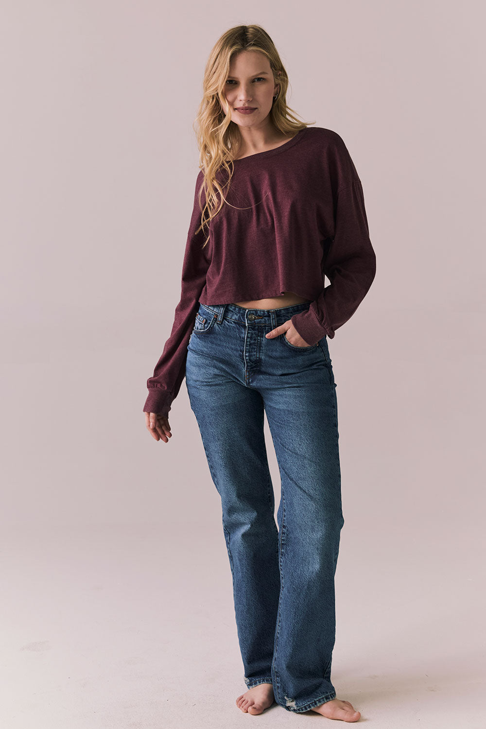 Full body view of model wearing the Hartt long sleeve tee in fig (deep purple) with clean silhouette and blue jeans, against a plain background.
