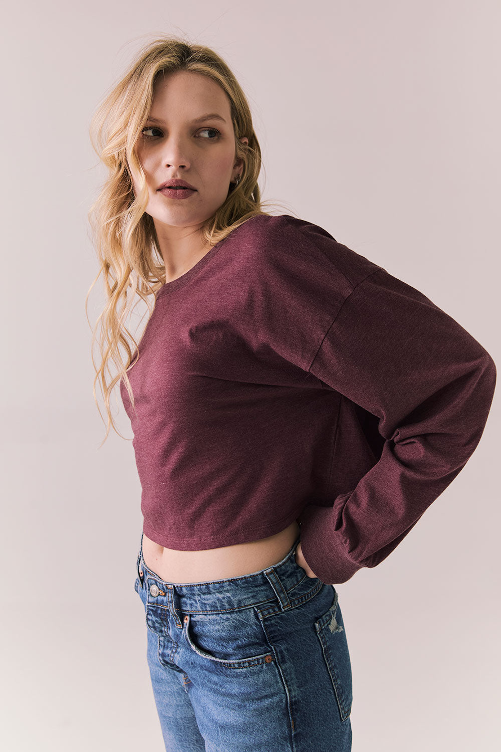 Side view of model wearing the Hartt long sleeve tee in fig (deep purple) with clean silhouette and blue jeans, against a plain background