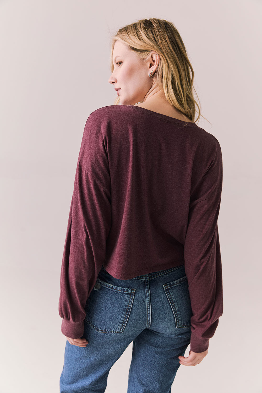 Back view of model wearing the Hartt long sleeve tee in fig (deep purple) with clean silhouette and blue jeans, against a plain background.