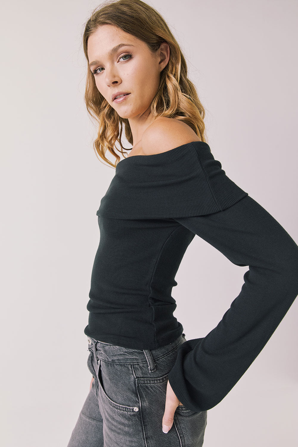 Side view of woman wearing Chaser’s Pixie True Black Long Sleeve with off-shoulder neckline on a white background
