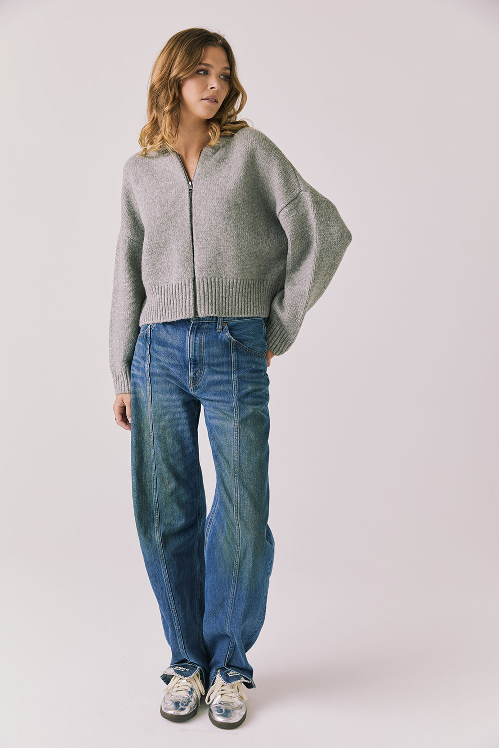 Full body view of woman wearing Chaser’s Heather Grey Luck Zip Up Cardigan Sweater and blue jeans on a white background