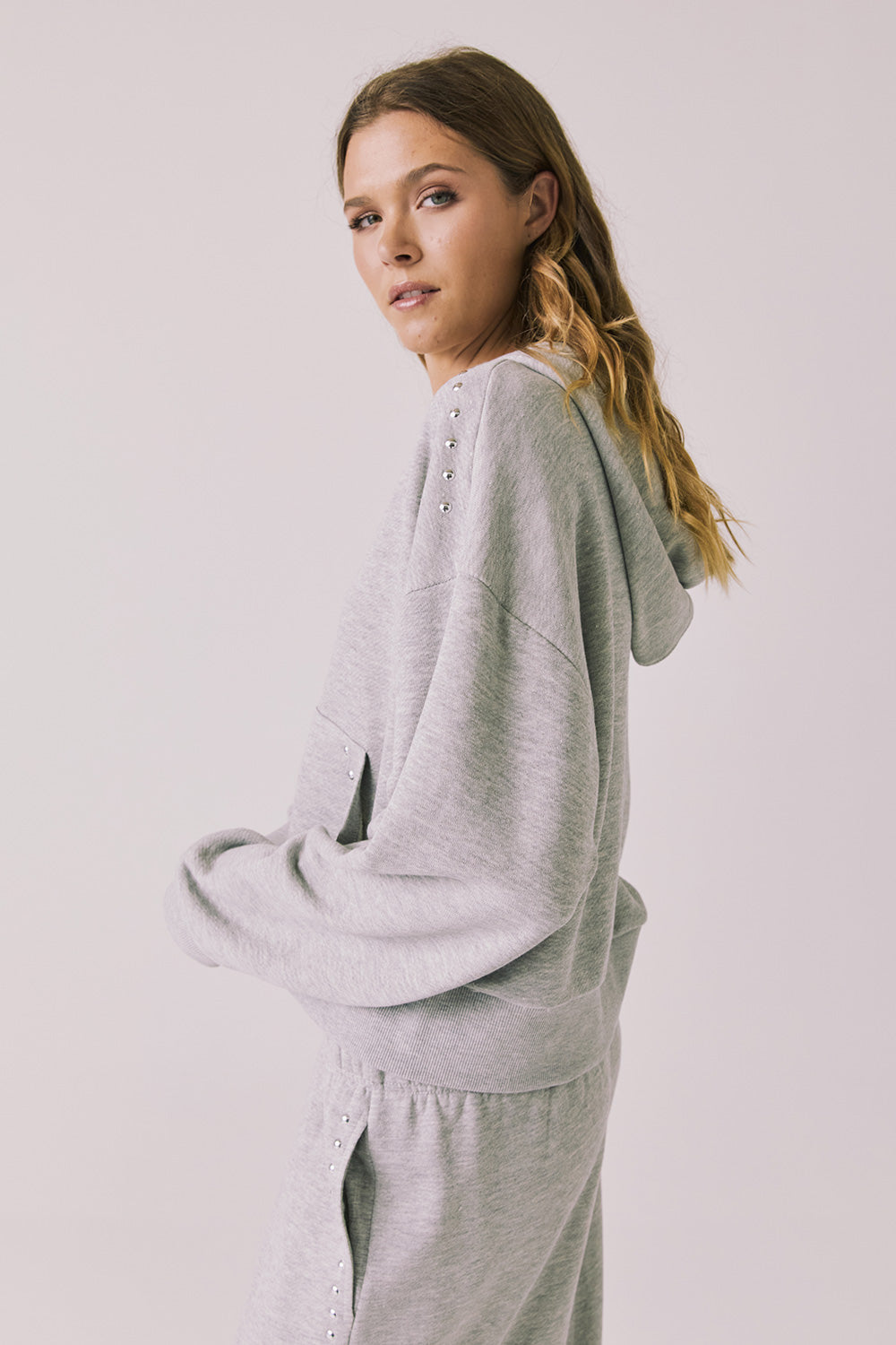 Side view of woman wearing Chaser’s Kiki Heather Grey Zip Up Hoodie with matching Daze Heather Grey Joggers on a white background