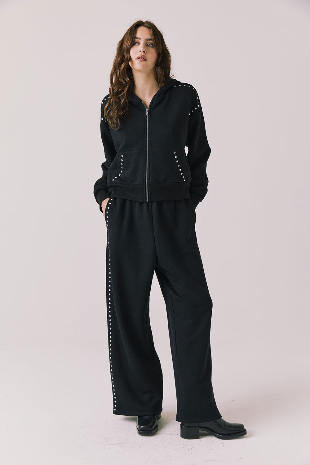 Full body view of woman wearing Chaser’s Kiki True Black Zip Up Hoodie with sequined shoulder accents and matching Daze True Black Joggers on a white background