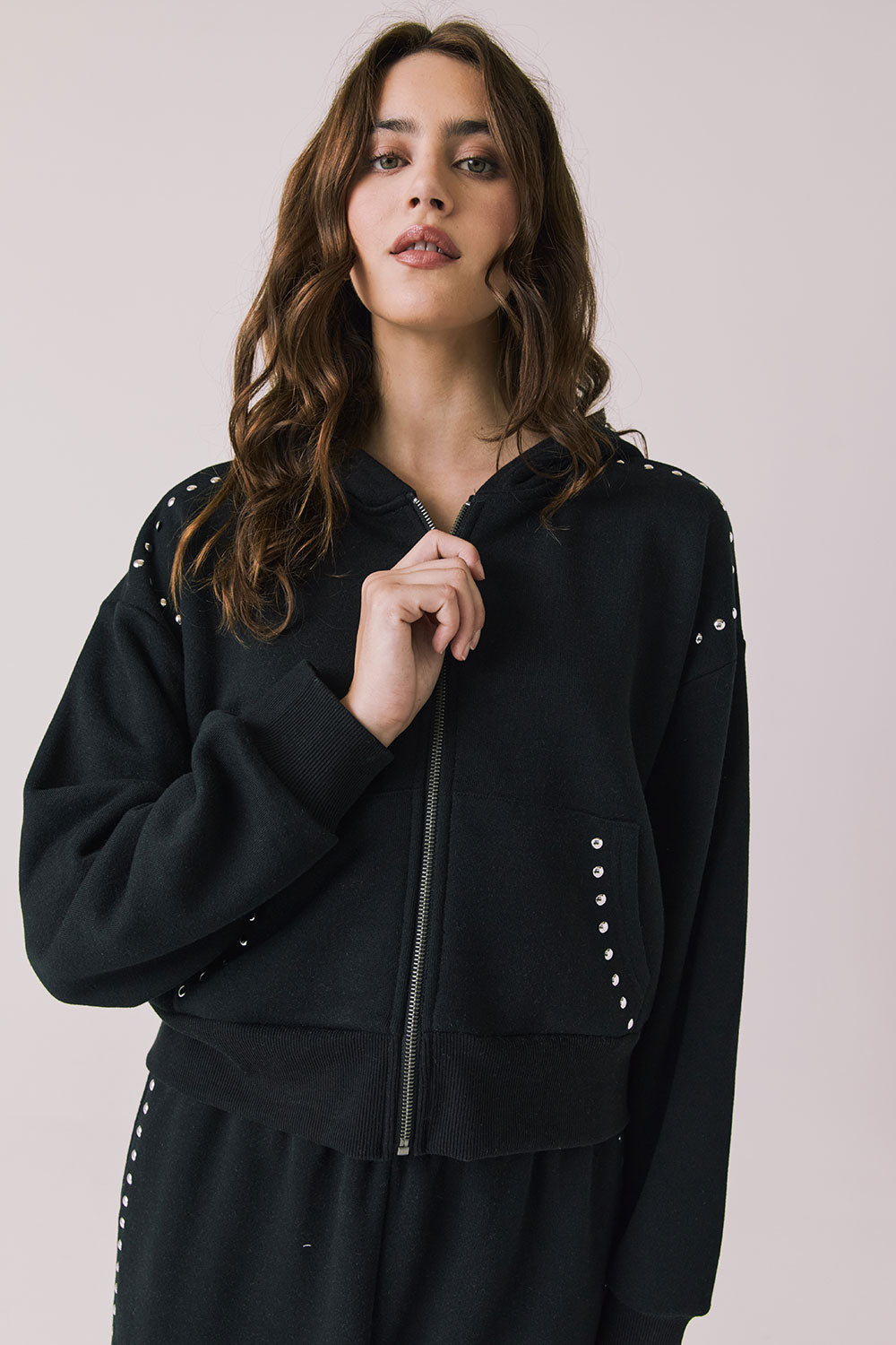 Front view of woman wearing Chaser’s Kiki True Black Zip Up Hoodie with sequin accents on the shoulders and pockets on a white background