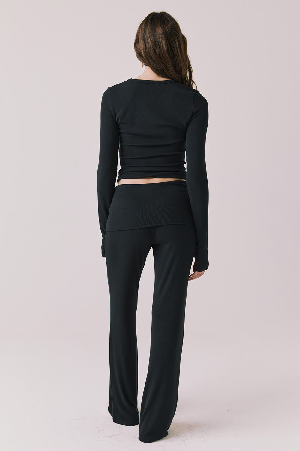 Full body back view of woman wearing Chaser’s True Black Mantra Legging with matching Porta True Black Long Sleeve on a plain background