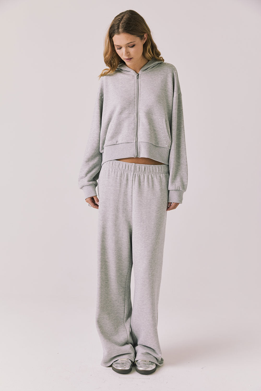 Full body view of woman wearing Chaser’s Daze Heather Grey Joggers and matching Kiki Heather Grey Zip Up Hoodie on a white background