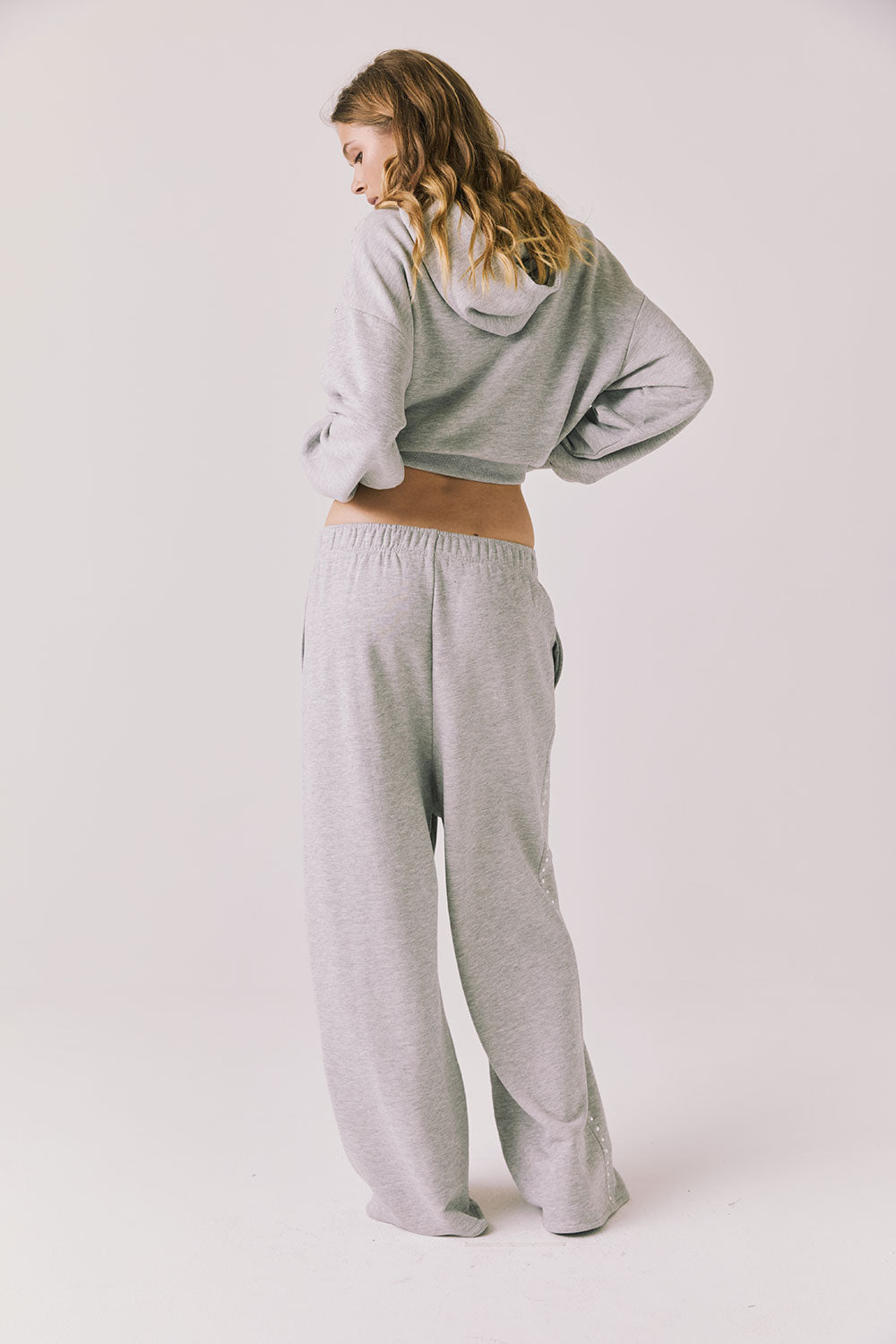 Full body back view of woman wearing Chaser’s Daze Heather Grey Joggers and matching Kiki Heather Grey Zip Up Hoodie on a white background