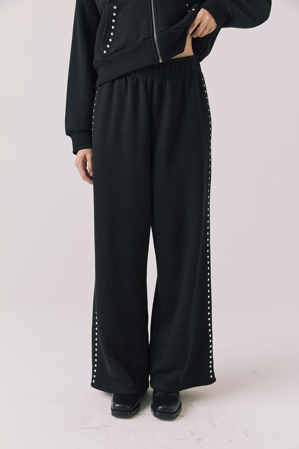 Front view of woman wearing Chaser’s Daze True Black Joggers with sequined button detailing on the pant seam on a white background