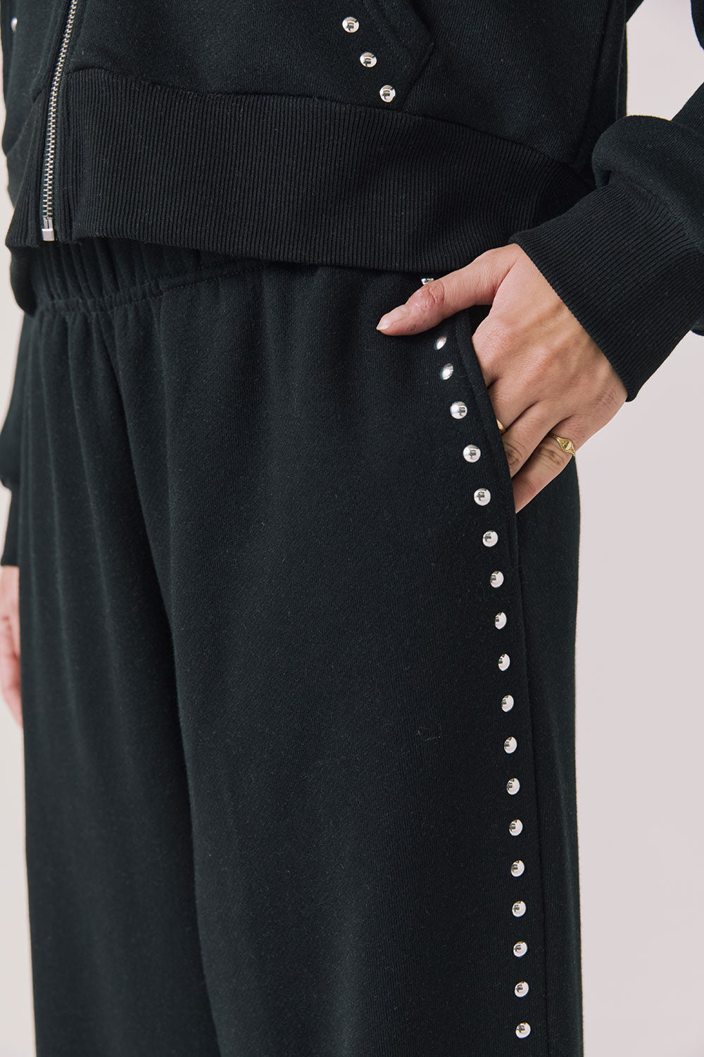 Side view of woman wearing Chaser’s Daze True Black Joggers with sequined button detailing on the pant seam on a white background