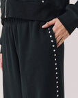 Side view of woman wearing Chaser’s Daze True Black Joggers with sequined button detailing on the pant seam on a white background
