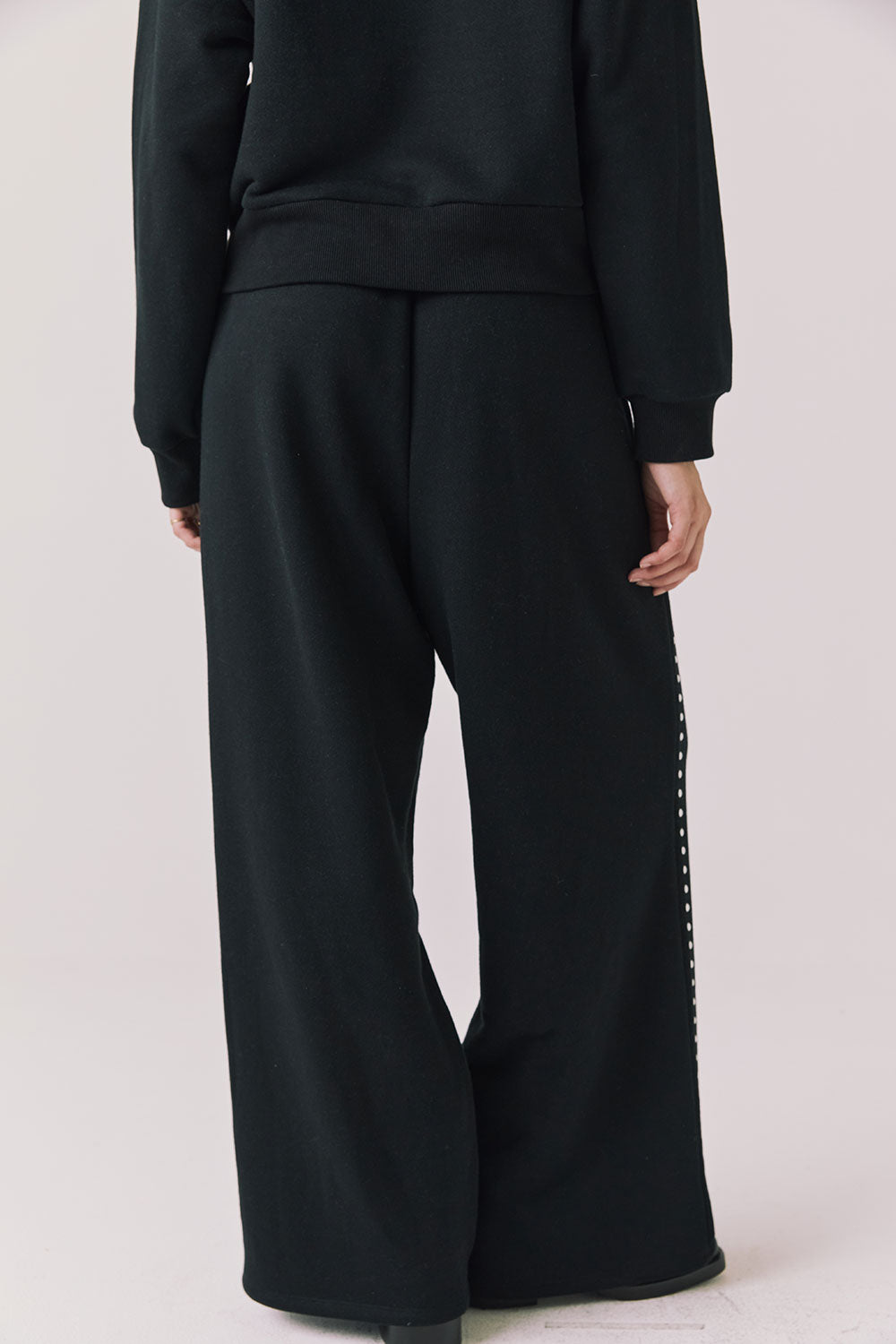 Back view of woman wearing Chaser’s Daze True Black Joggers with sequined button detailing on the pant seam on a white background