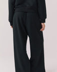 Back view of woman wearing Chaser’s Daze True Black Joggers with sequined button detailing on the pant seam on a white background