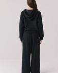 Full body back view of woman wearing Chaser’s Daze True Black Joggers and matching Kiki True Black Zip Up Hoodie with sequin details on a white background