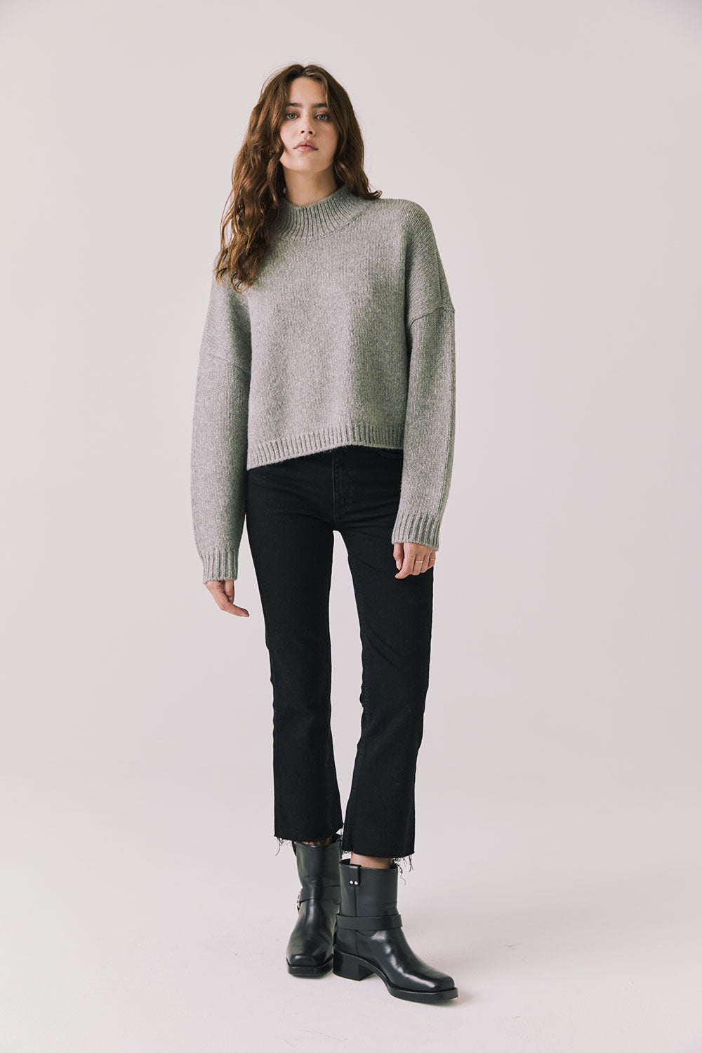 Full body view of woman wearing Chaser’s Frankie Heather Grey Pullover Sweater with black pants and black boots on a white background