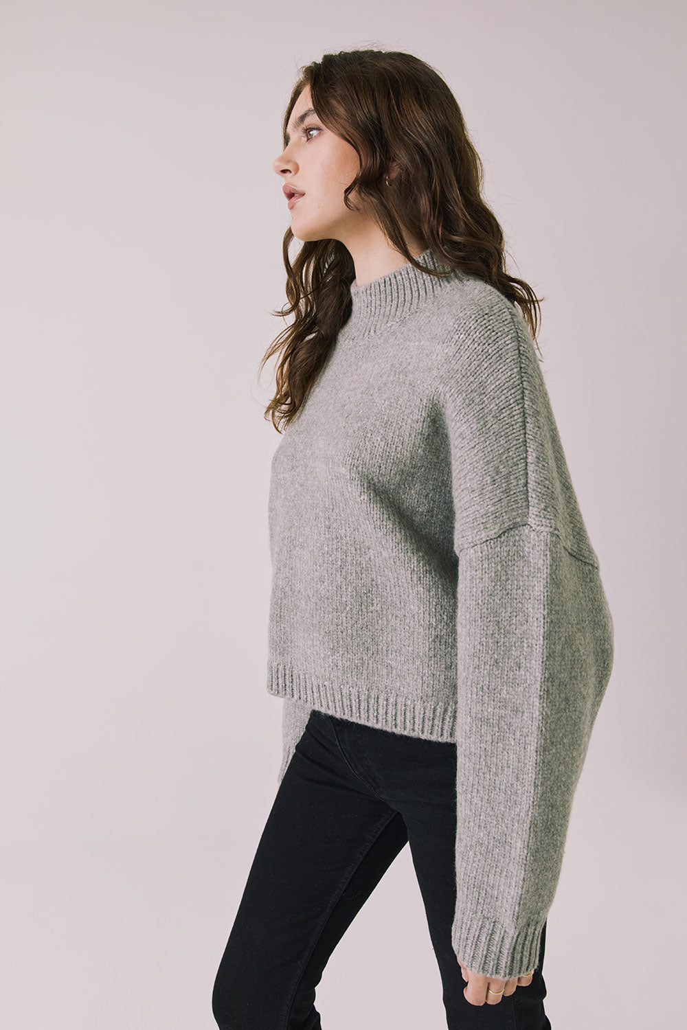Side view of woman wearing Chaser’s Frankie Heather Grey Pullover Sweater with black pants on a white background