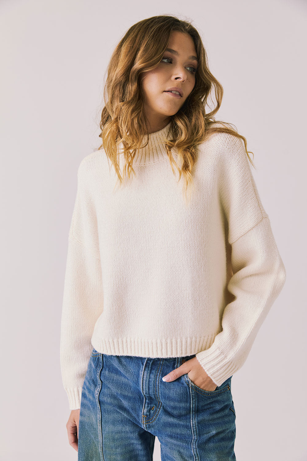 Front view of woman wearing Chaser’s Frankie Warm White Pullover Sweater with blue jeans on a white background