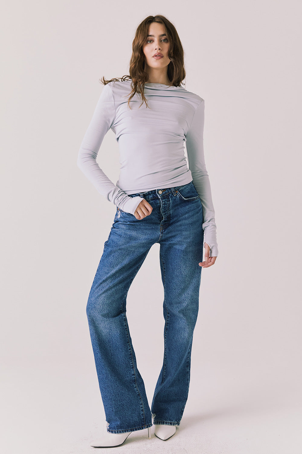 Full body view of woman wearing Chaser’s Owen Moonstone Grey Long Sleeve top and blue jeans on a light gray background