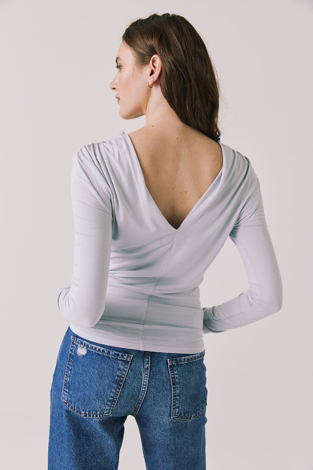  Back view of woman wearing Chaser’s Owen Moonstone Grey Long Sleeve top featuring a low-cut open back design on a light gray background