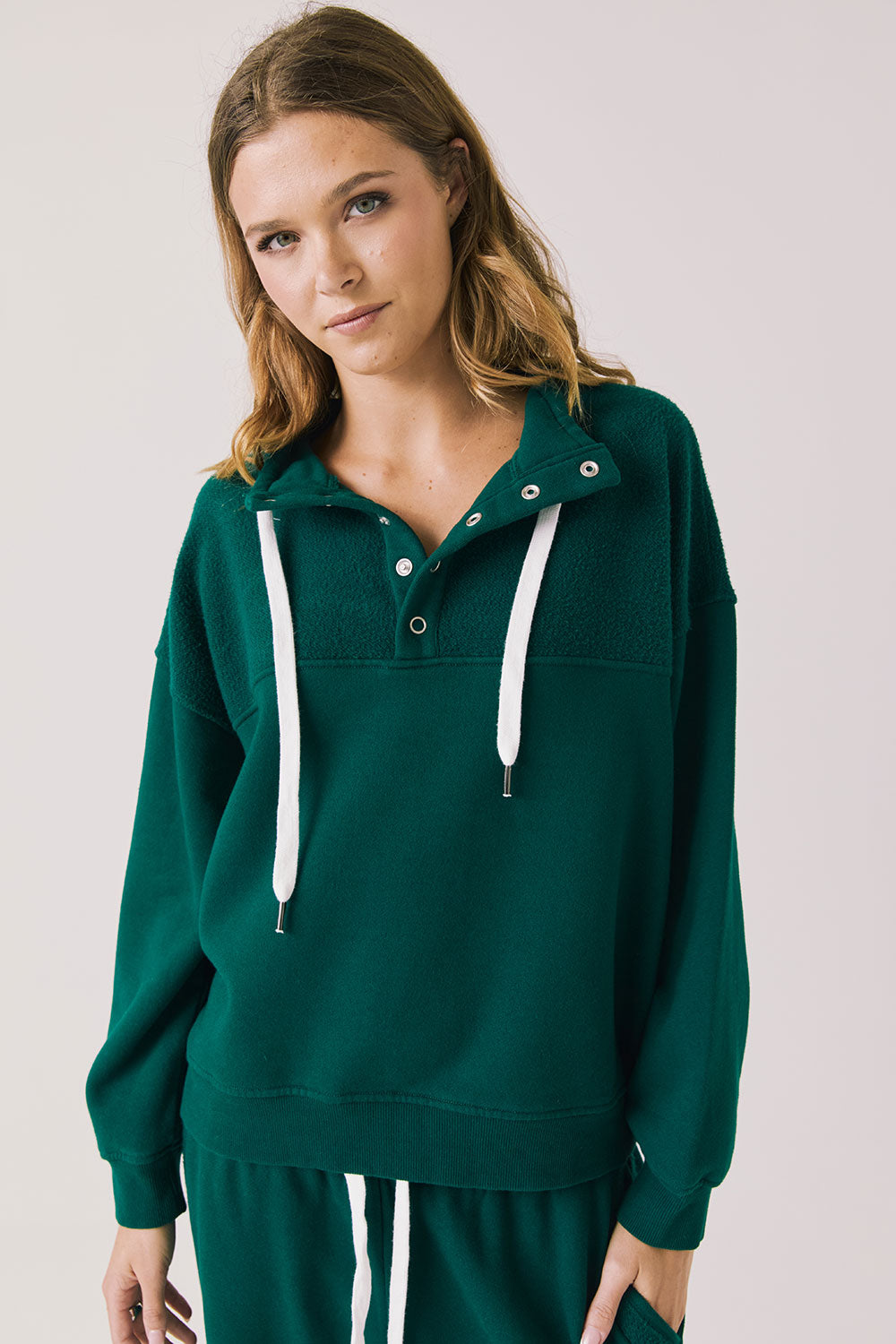 Front view of woman wearing Chaser’s City Blue Grass Green Half Zip Pullover with white drawstrings on a plain background