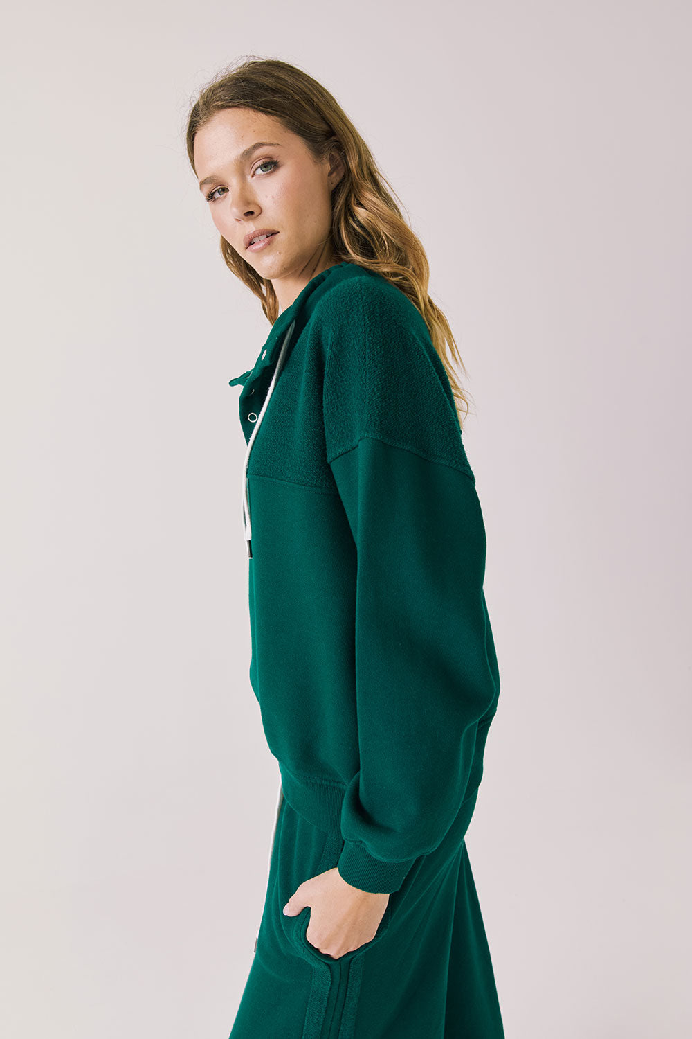 Side view of woman wearing Chaser’s City Blue Grass Green Half Zip Pullover with white drawstrings on a plain background