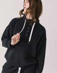 Front view of woman wearing Chaser’s City True Black Half Zip Pullover with white drawstrings on a plain background