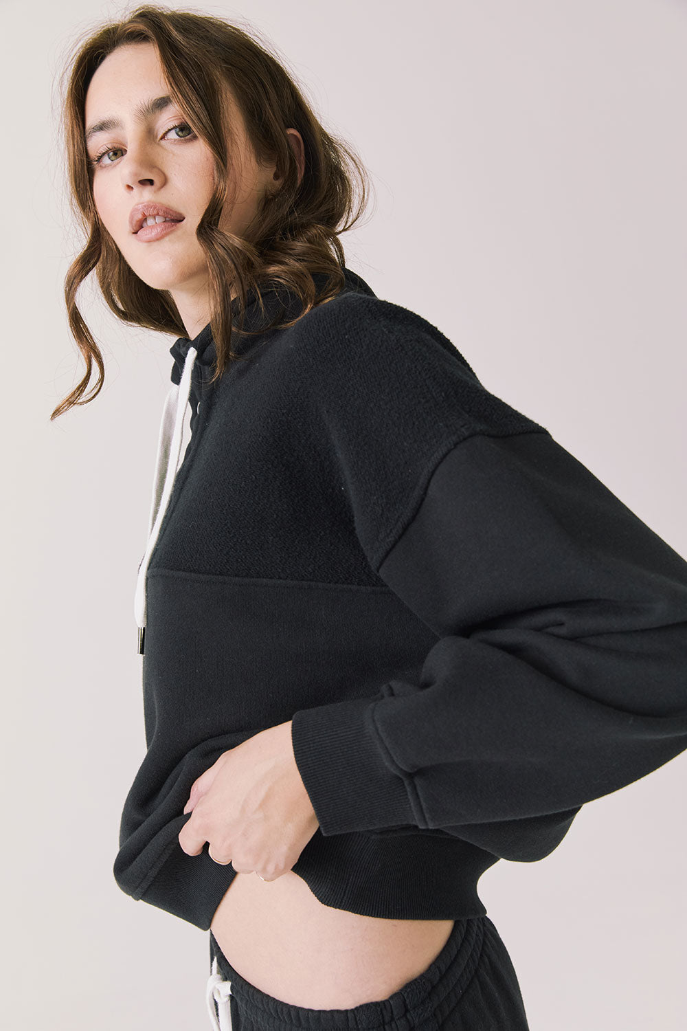 Side view of woman wearing Chaser’s City True Black Half Zip Pullover with white drawstrings on a plain background