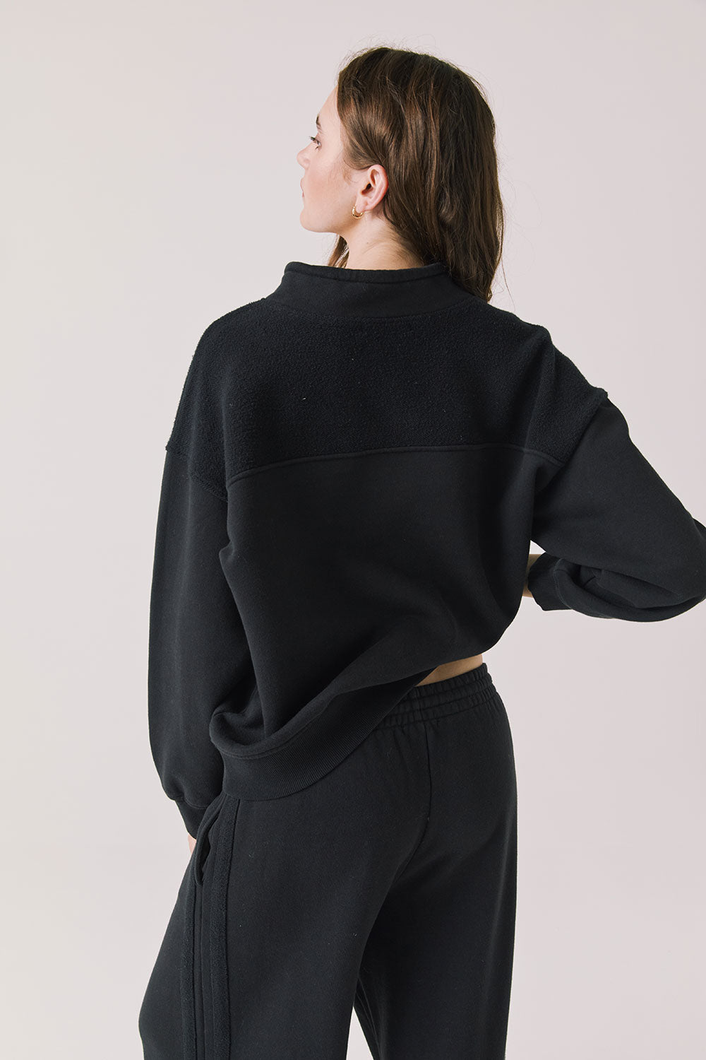 Back view of woman wearing Chaser’s City True Black Half Zip Pullover with white drawstrings on a plain background