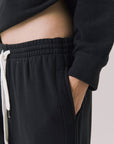 Side view of woman wearing Chaser’s Hazel Joggers in true black with hand in pocket on a white background