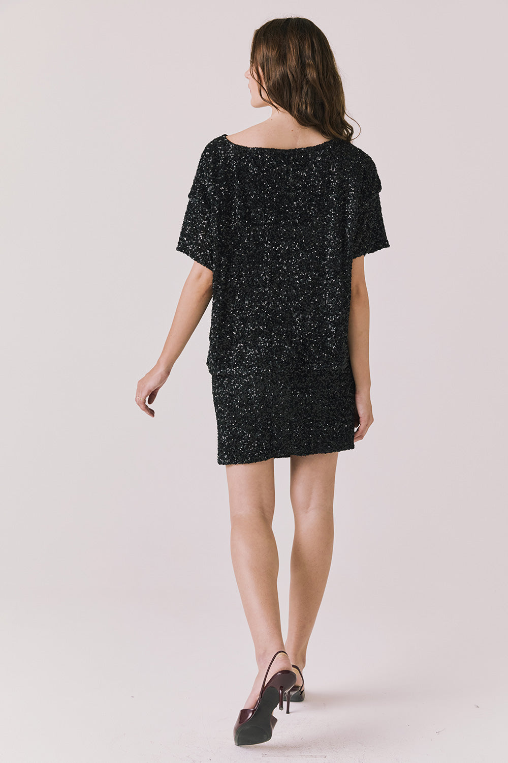 Full body back view of woman wearing Chaser’s Jayde True Black Mini Skirt with matching Davis True Black Tee on a light gray background
