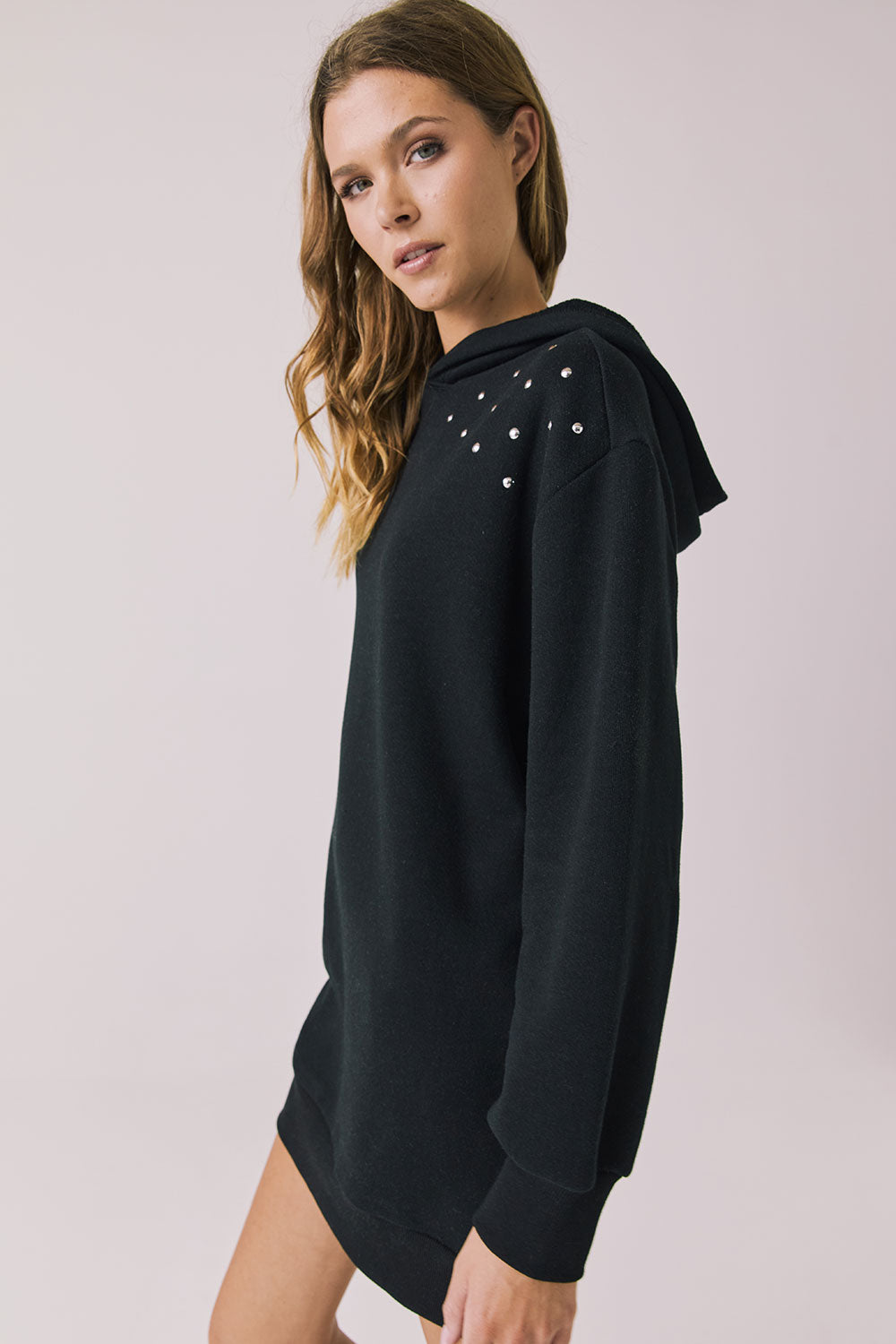 Side view of woman wearing Chaser Aster True Black Hoodie Dress with decorative elements on shoulders on a plain background