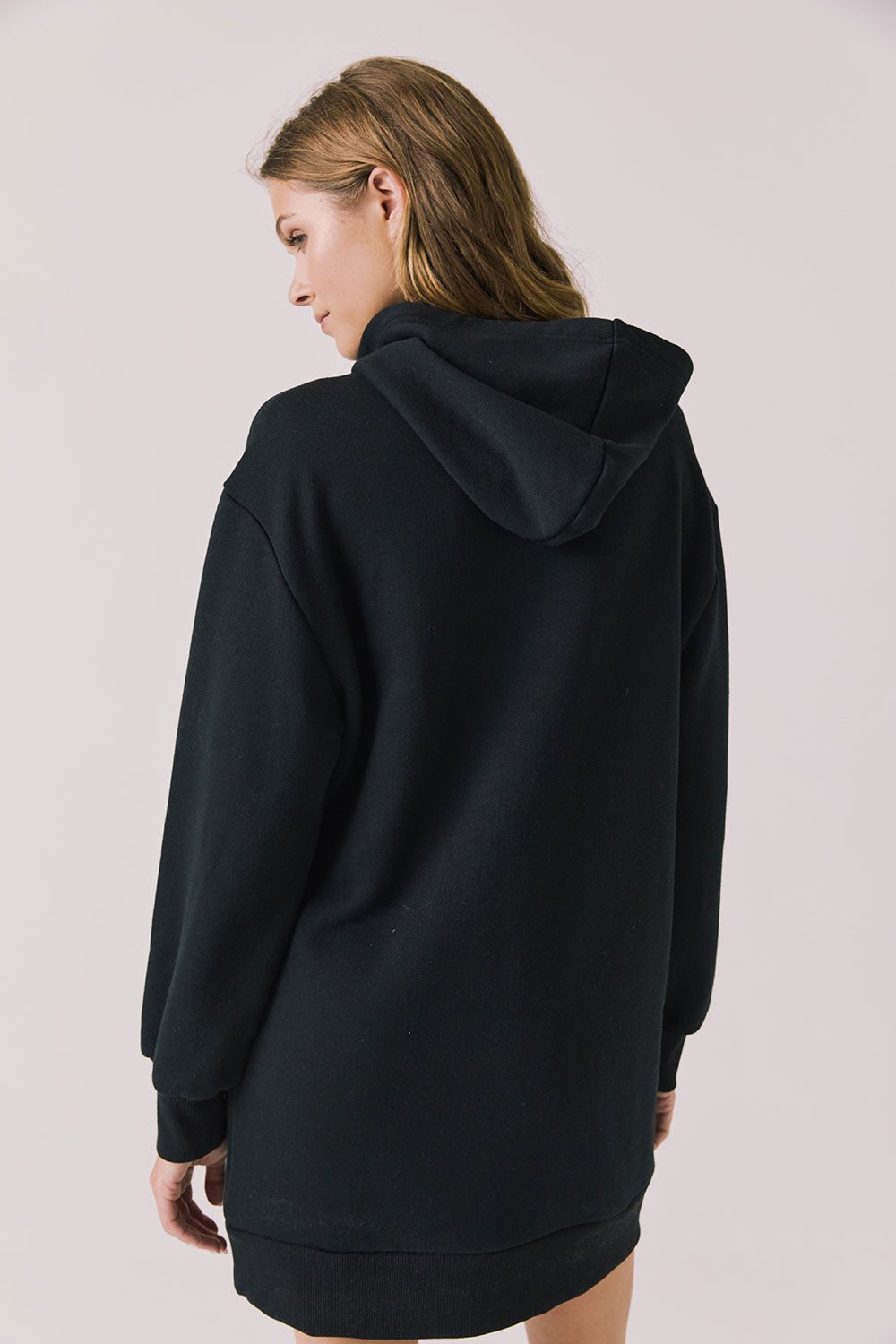 Back view of woman wearing Chaser Aster True Black Hoodie Dress on a plain background