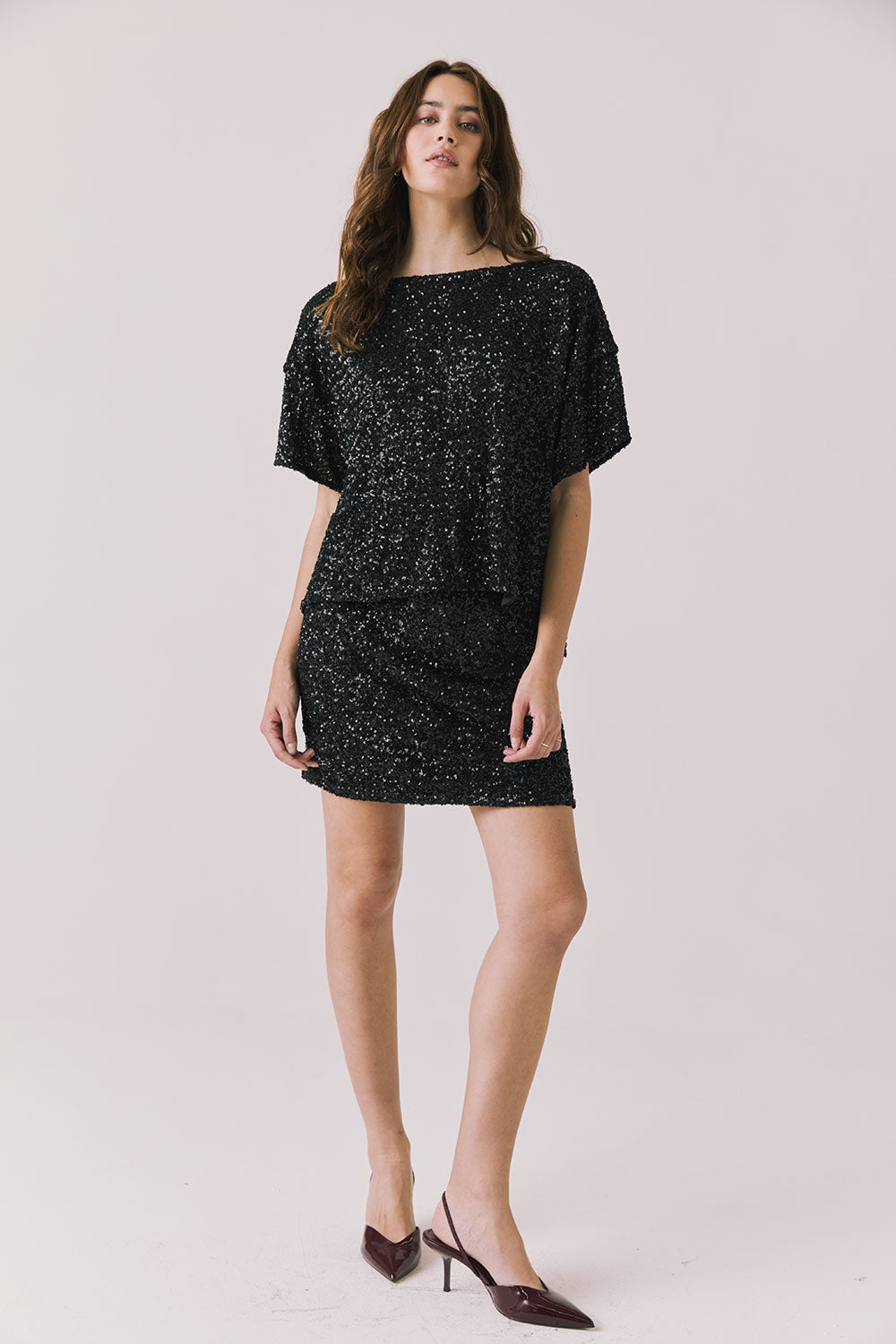 Full body view of woman wearing Chaser’s Davis True Black Tee and matching Jayde True Black Mini Skirt on a light gray background