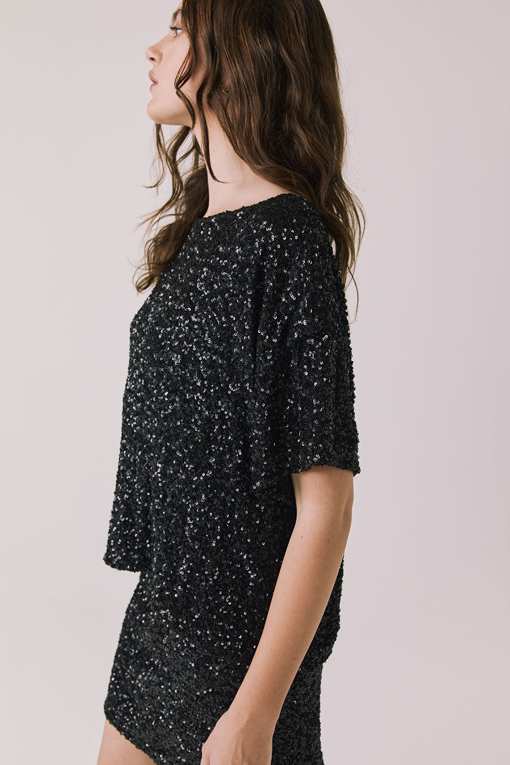 Side view of woman wearing Chaser’s Davis True Black Tee and matching Jayde True Black Mini Skirt on a light gray background