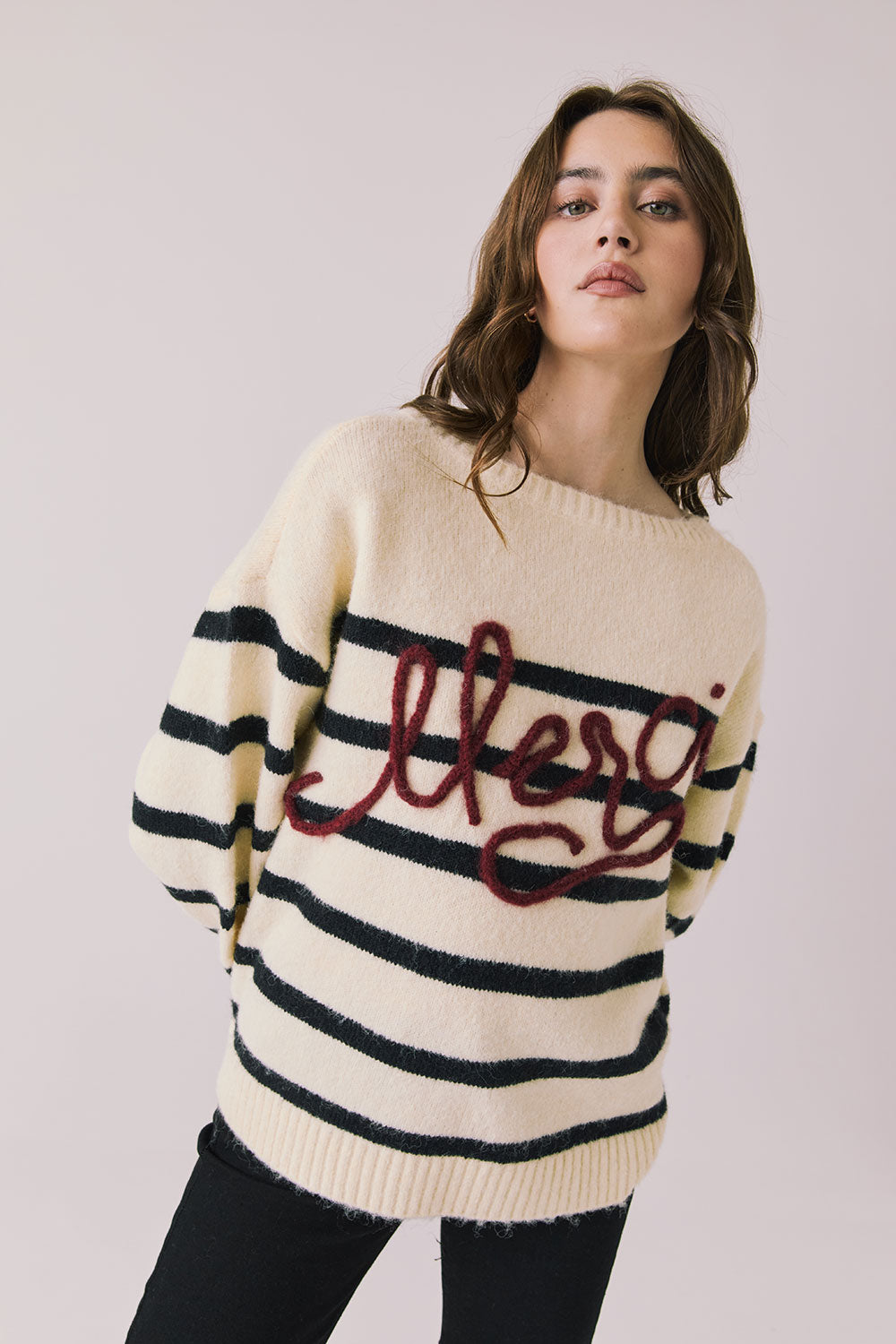Front view of woman wearing Chaser’s striped Merci Long Sleeve Sweater with “merci” burgundy red text on a white background
